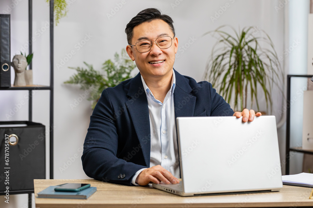 Portrait of happy Asian businessman freelancer at home office modern workplace working on laptop computer. Manager Chinese man in formal suit work on notebook send messages makes online purchases Portrait of happy Asian businessman freelancer at home office modern workplace working on laptop computer. Manager Chinese man in formal suit work on notebook send messages makes online purchases