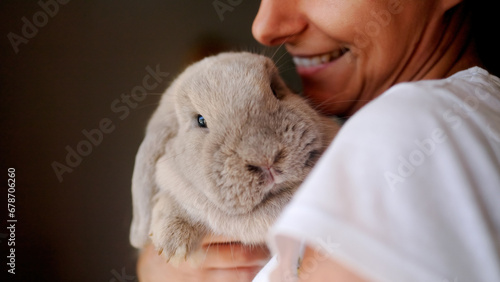 Happy woman holding bunny rabbit indoors at home. Pet animals relationship concept