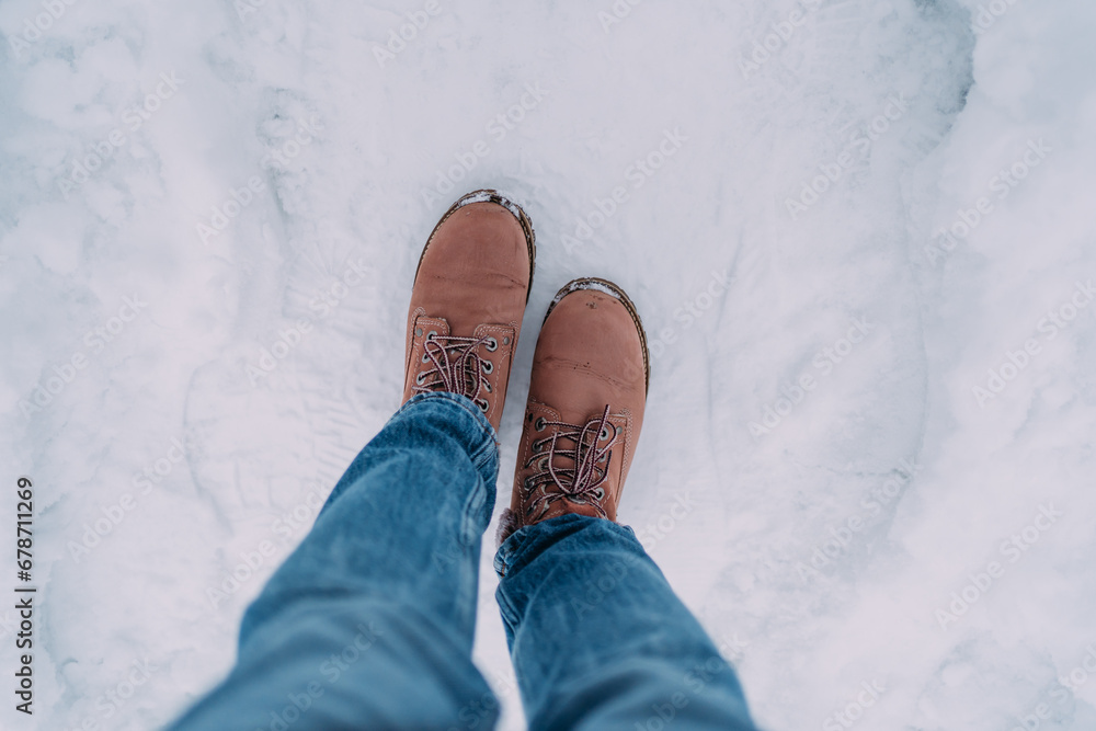 Women's feet in pink Timberland boots in the snow. The woman is wearing blue jeans. Only boots and snow are visible