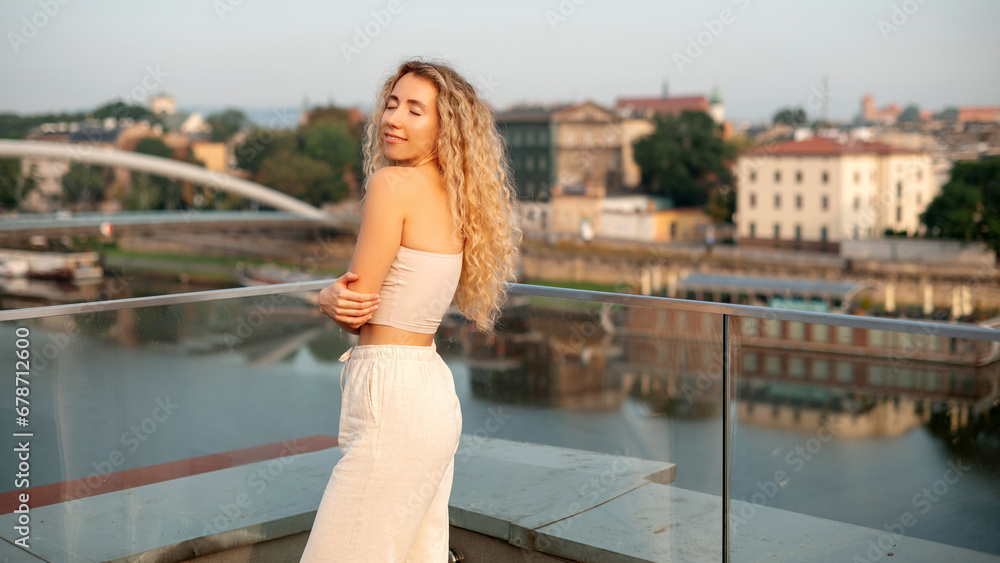 Happy smiling girl with long curly hair posing on the rooftop with city background