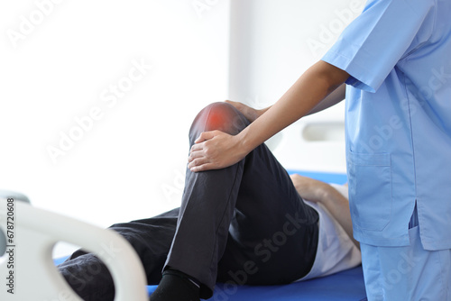 Nurse doing leg and knee physiotherapy to male patient in hospital examination room.