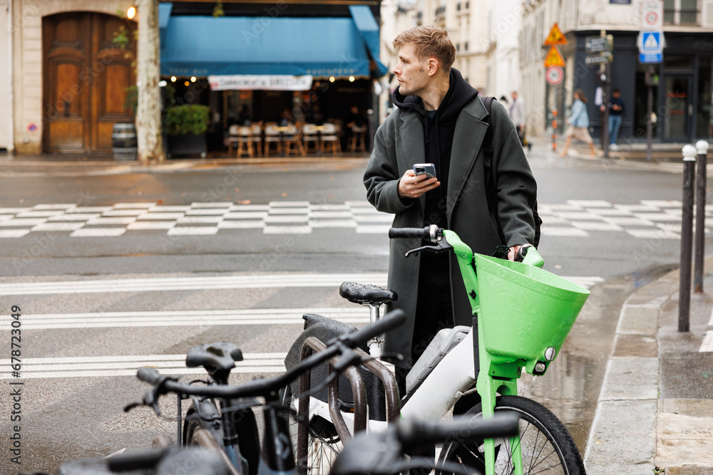 Obraz premium Micromobility ecology. Green sustainable mobility Young man unlocks an e-scooter with his mobile phone. Electric scooter new way city. Green transportation. Sustainable climate neutral cities goals. 