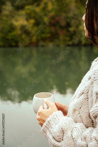 woman holding a cup of coffee close to her heart by the river