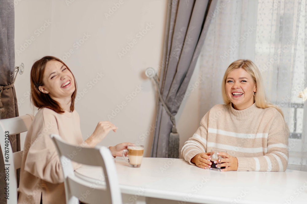 two women friends at the table drinking coffee and talking in a bright room. female friendship concept