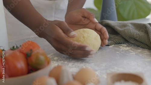 Close up shot of bakery woman worker carefuly forming and turning loafs of dough for bread or pasta. Dark skin woman making dough, using natural ingredients. food and drink 4k footage. photo