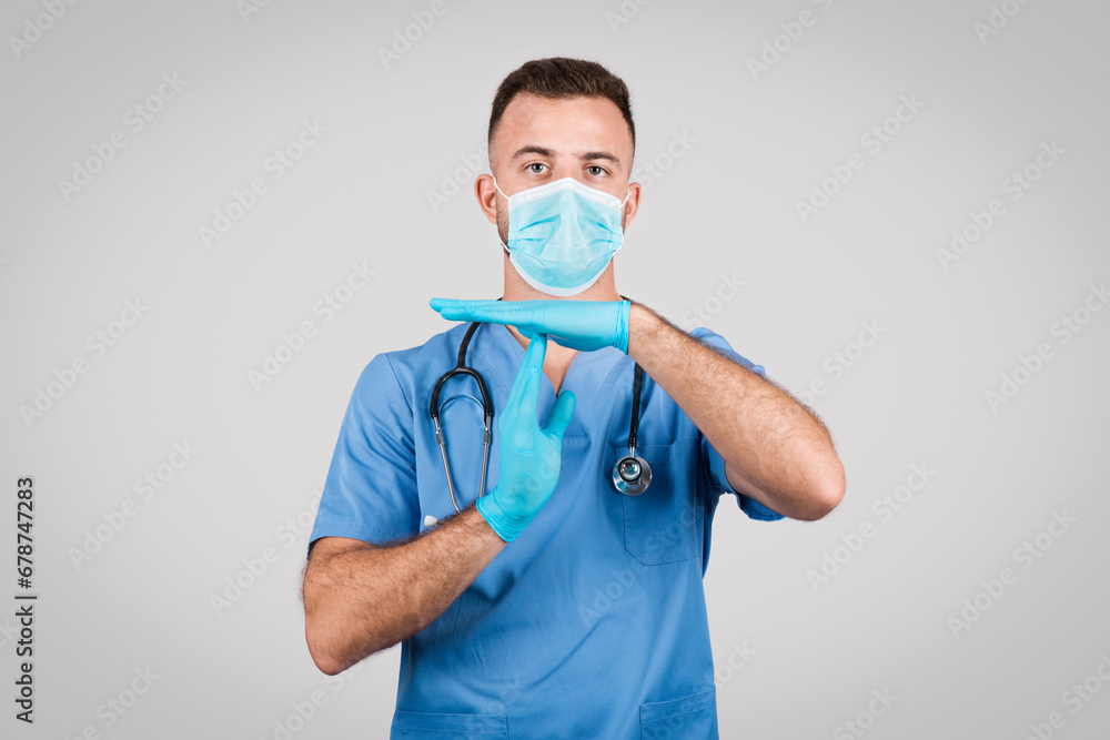 Male nurse in scrubs with mask gesturing timeout