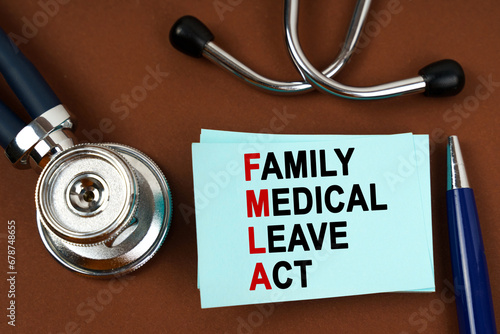 On a brown surface there is a stethoscope, a pen and blue stickers with the inscription - family medical leave act photo