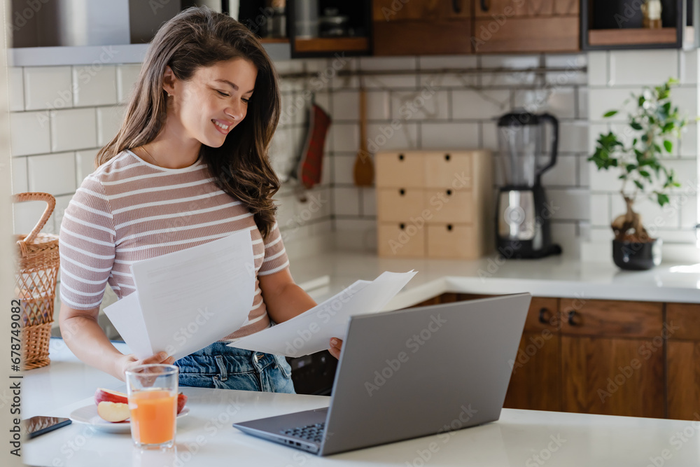 Young beautiful entrepreneur women started working from home, looking at papers and using laptop computers in the kitchen during breakfast Young beautiful entrepreneur women started working from home, looking at papers and using laptop computers in the kitchen during breakfast