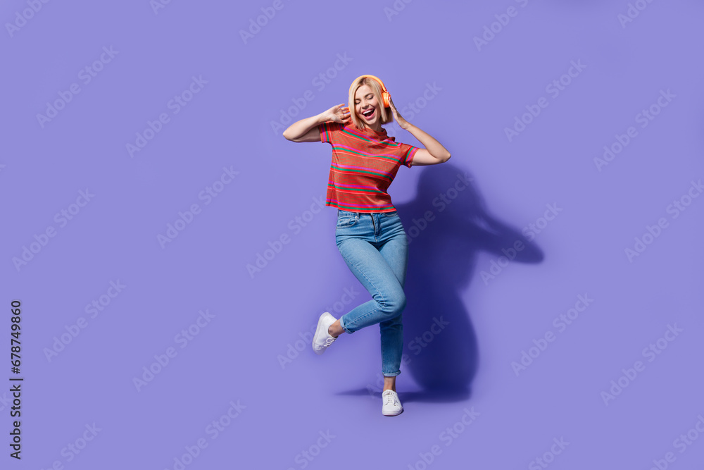 Full length photo of good mood girl bob blonde hair dressed t shirt with jeans touch earphones while dance isolated on purple background