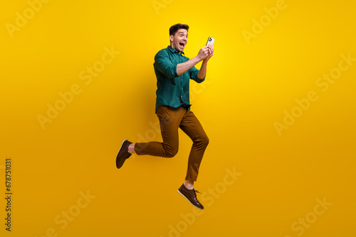 Photo of cheerful positive excited man dressed trendy outfit reading instagram telegram twitter post isolated on yellow color background