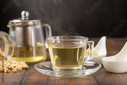 Relaxing chamomile tea in glass cup with lemon slices and honey next to it on wooden table.