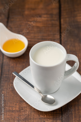 Milk in a porcelain cup and honey in a porcelain bowl on a wooden table