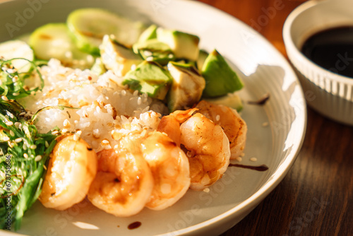 Light snack of avocado and shrimp on a round plate on a wooden table.