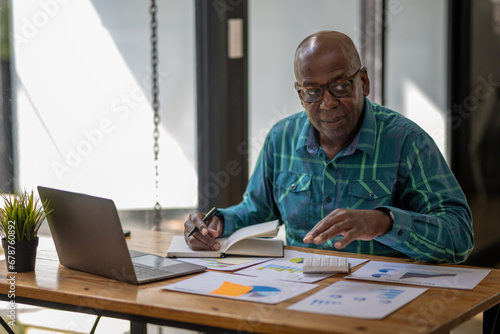 Black senior man in casual clothes carefully reviews project work and performance for continuous growth and development.