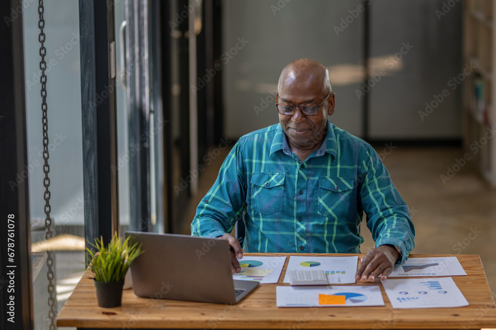 A senior black man in casual clothes is busy at work but happy with the work and paperwork in front of him. A senior black man in casual clothes is busy at work but happy with the work and paperwork in front of him.