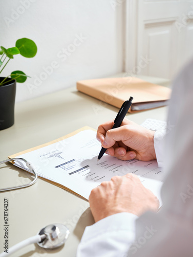 Unrecognizable male doctor in a white gown filling out medical documentation in a clinic