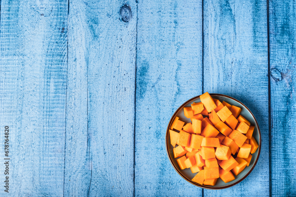 Pumpkin pieces in a bowl on a wooden blue background. Place for text.