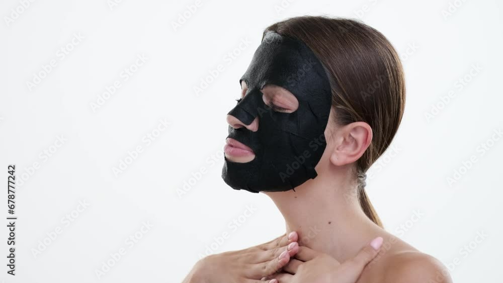Caucasian woman wears a black facial mask, eyes reflecting a sense of tranquility and self care against a clean white backdrop. The mask enhances her features, highlighting the dedication to skincare. Caucasian woman wears a black facial mask, eyes reflecting a sense of tranquility and self care against a clean white backdrop. The mask enhances her features, highlighting the dedication to skincare.