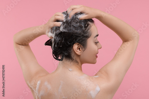 Woman washing hair on pink background, back view