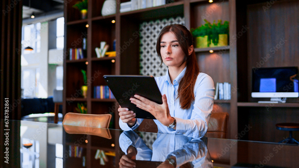 Successful Caucasian woman working at office desk using tablet online. Smart and focused young woman in formal attire is busy working in the company. CEO concept. Successful Caucasian woman working at office desk using tablet online. Smart and focused young woman in formal attire is busy working in the company. CEO concept.