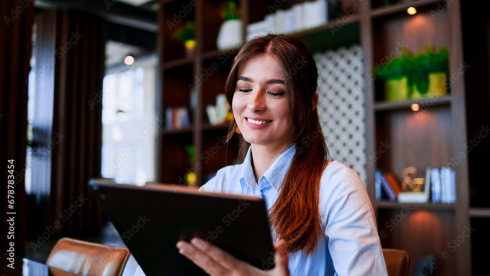 Portrait of beautiful female manager sitting at work place and using digital tablet indoors. Attractive and elegant businesswoman working in modern urban office. Business, office, coworking space.