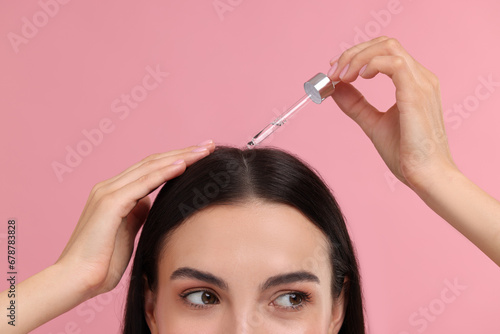Woman applying hair serum on pink background, closeup. Cosmetic product photo