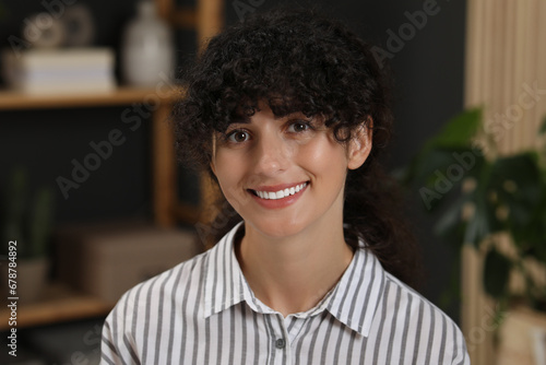 Portrait of beautiful woman with curly hair indoors. Attractive lady smiling and looking into camera