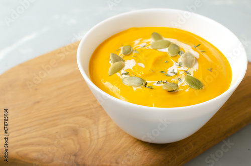 One white bowl of pumpkin cream soup with dried seeds and thyme leaves on a wooden cutting board on a gray background. Concept of healthy eating. Vegetarian and vegan food. Horizontal orientation.