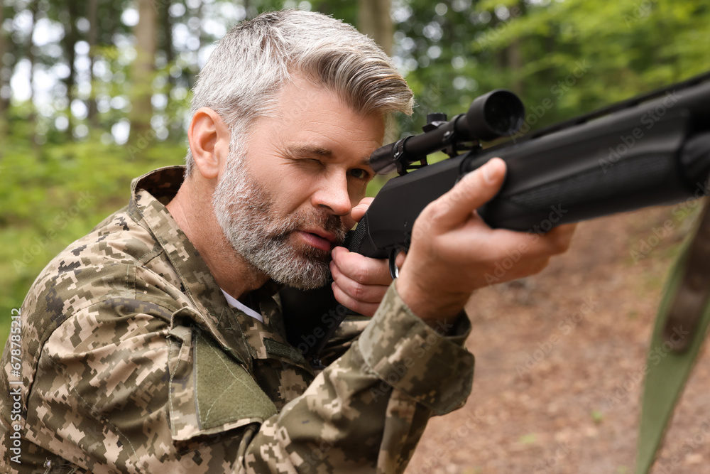 Man wearing camouflage and aiming with hunting rifle in forest