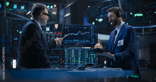 Two Successful Traders Analyzing Real-Time Financial Data and Reports About the State of the Finance Market. Stock Exchange Professionals Discussing Buy and Sell Options For Different Bonds photo
