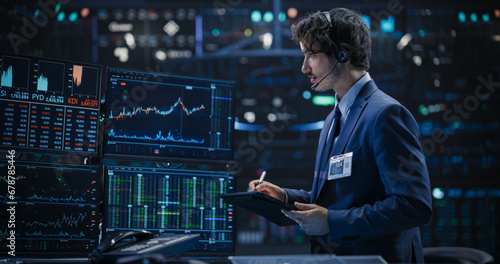 Portrait of a Young Man Working in an International Stock Exchange Company: Professional Using a Tablet Computer, Monitoring Financial Markets, Communicating with Corporate Business Partners photo