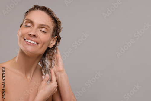 Portrait of beautiful happy woman washing hair on light grey background. Space for text