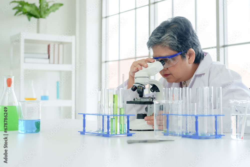 Elderly female science teacher nearing retirement primary school Prepare science test tubes to teach elementary school students. Scientist in white uniform sitting at table in laboratory Elderly female science teacher nearing retirement primary school Prepare science test tubes to teach elementary school students. Scientist in white uniform sitting at table in laboratory