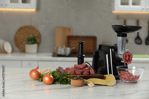 Electric meat grinder with beef mince and products on white table in kitchen
