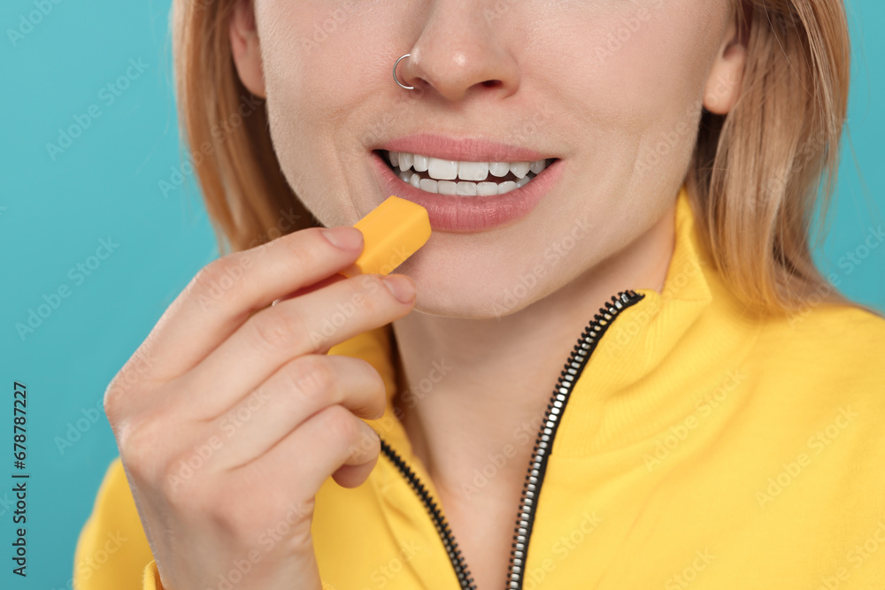 Obraz na plátně Woman putting bubble gum into mouth on light blue background, closeup