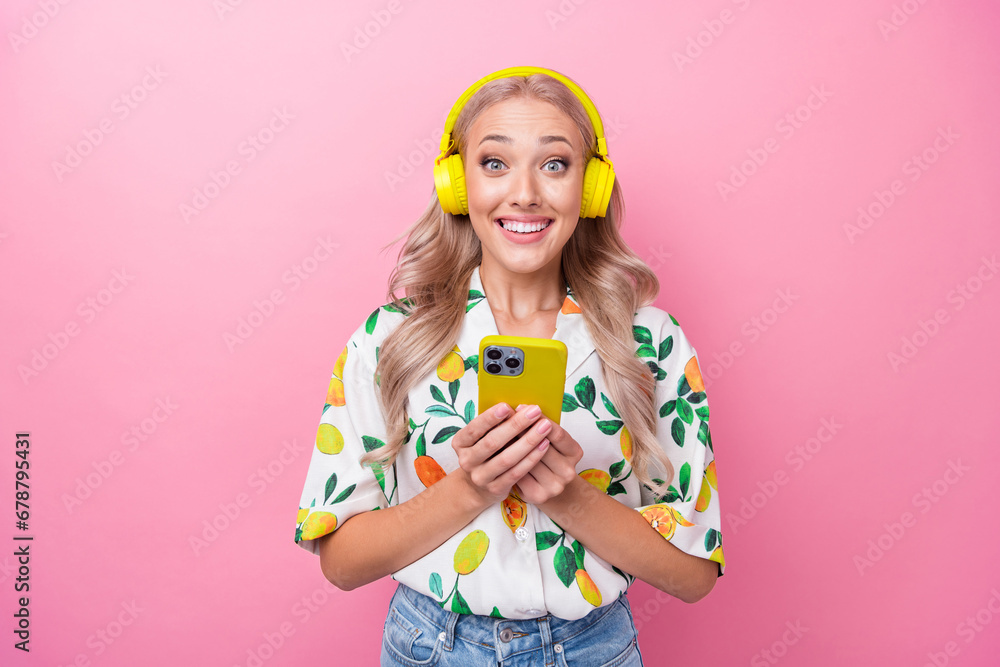 Photo of impressed overjoyed girl dressed flower print blouse listen music in headphones hold smartphone isolated on pink color background Photo of impressed overjoyed girl dressed flower print blouse listen music in headphones hold smartphone isolated on pink color background