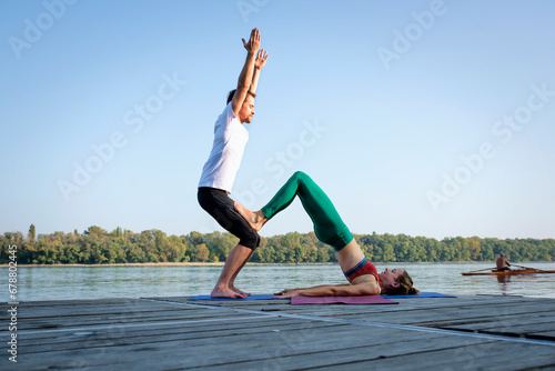 Couple practicing yoga on wooden deck by the river