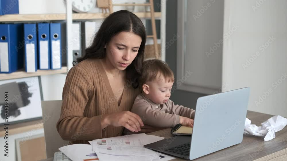 Amidst the hum of productivity, a cheerful mother balances professional duties on a laptop while cradling little son in arms. Her face radiates warmth and happiness, mirroring the joy of motherhood. Amidst the hum of productivity, a cheerful mother balances professional duties on a laptop while cradling little son in arms. Her face radiates warmth and happiness, mirroring the joy of motherhood.