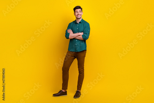 Full length photo of responsible worker nice man standing with crossed arms watching up empty space isolated on yellow color background
