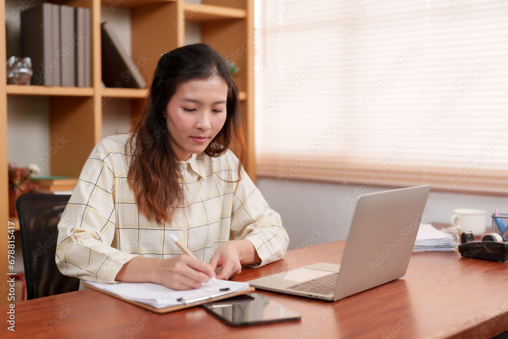 Office woman sitting working in front computer screen placed on table in front, eyes turned look at work information in document placed near computer, check work see if information matches or not. Office woman sitting working in front computer screen placed on table in front, eyes turned look at work information in document placed near computer, check work see if information matches or not.