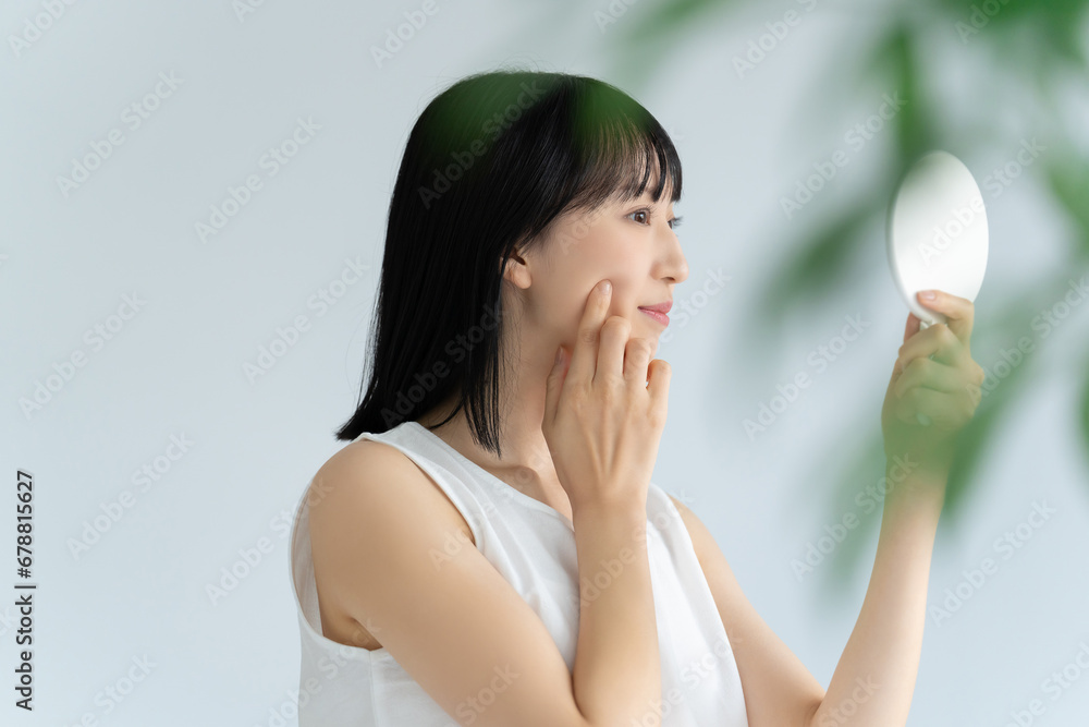 鏡で肌をチェックする白い服の若い女性