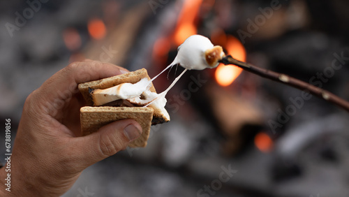 Closeup hand roasting marshmallow enjoying s'more by a campfire. Camping cooking concept.	
 photo