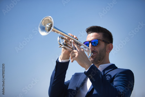 Young Hispanic man  wearing a jacket and sunglasses  playing a pretty  silvery trumpet outdoors. Concept  music  instruments  trumpet.