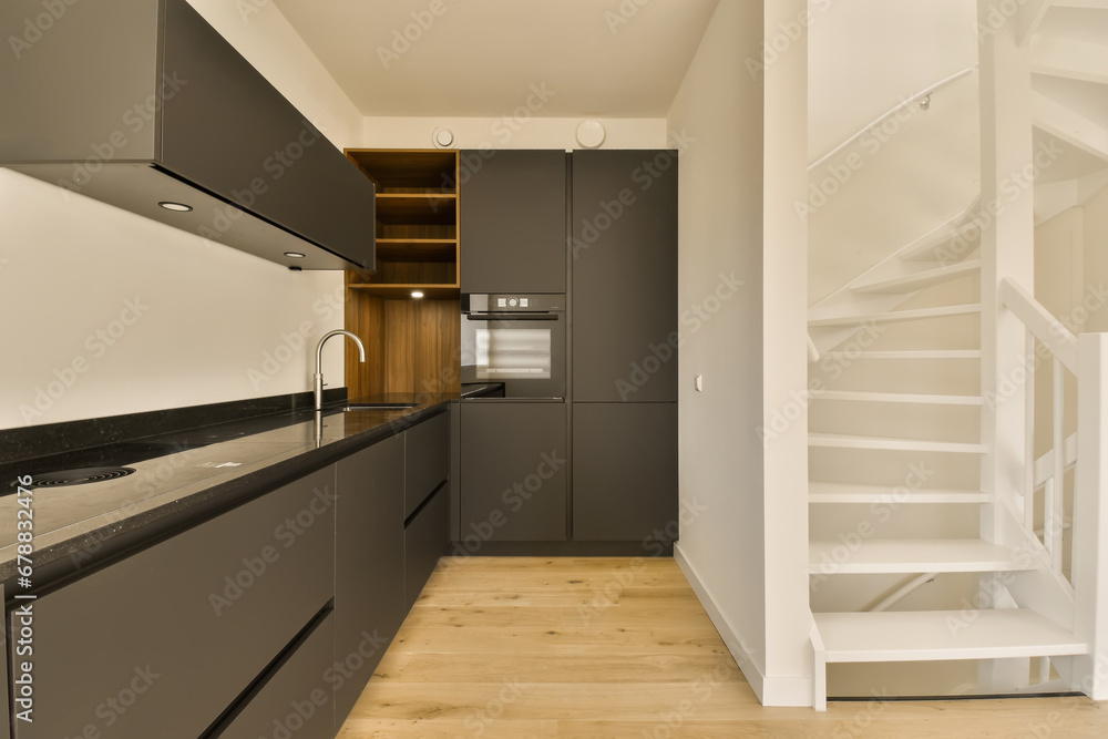 a modern kitchen and staircase in a house with white walls, wood flooring and dark grey cabinetd cupboards a modern kitchen and staircase in a house with white walls, wood flooring and dark grey cabinetd cupboards