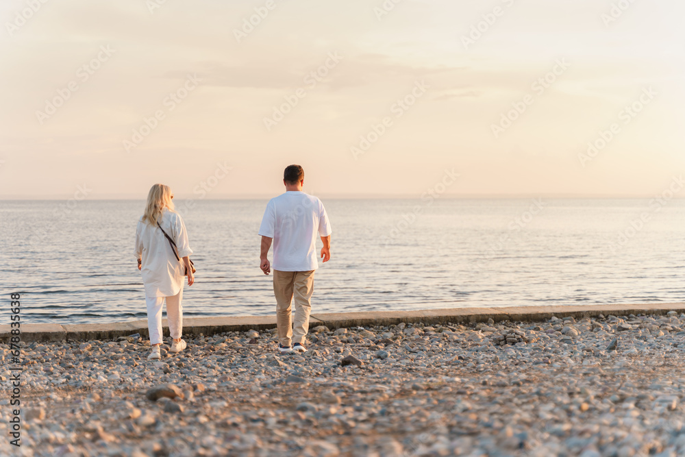 A charming couple in a white shirt walks along the shore at sunset in summer,rear view. Togliatti, Russia - 15 Aug 2023