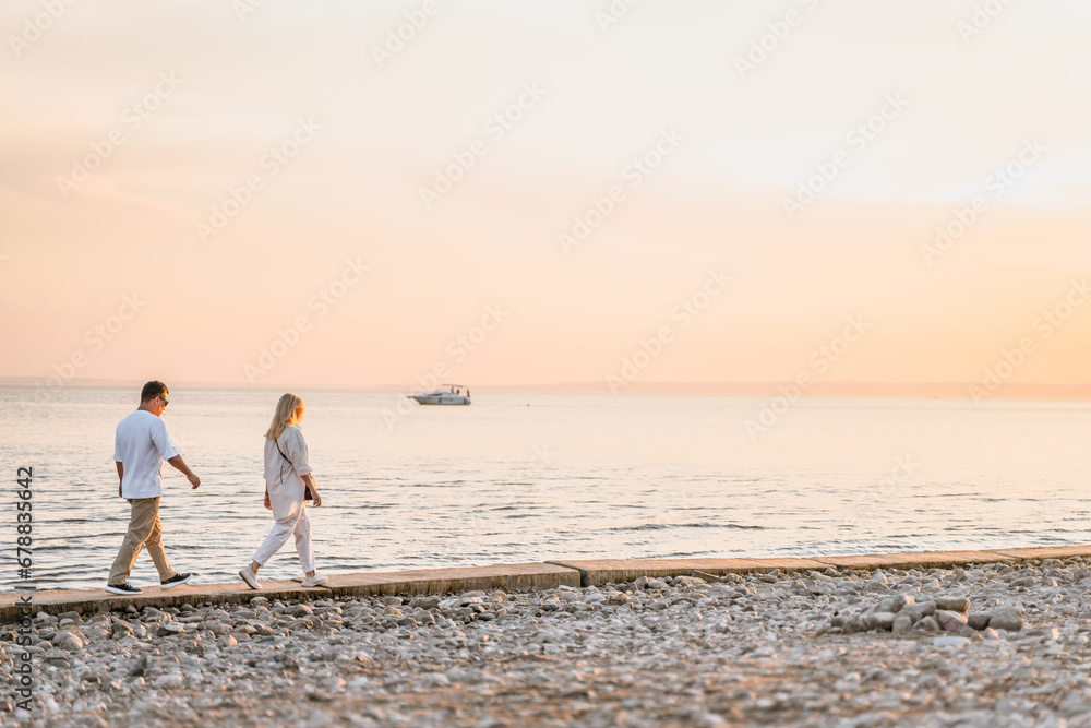 A charming couple in a white shirt walks along the shore at sunset in summer,rear view. Togliatti, Russia - 15 Aug 2023