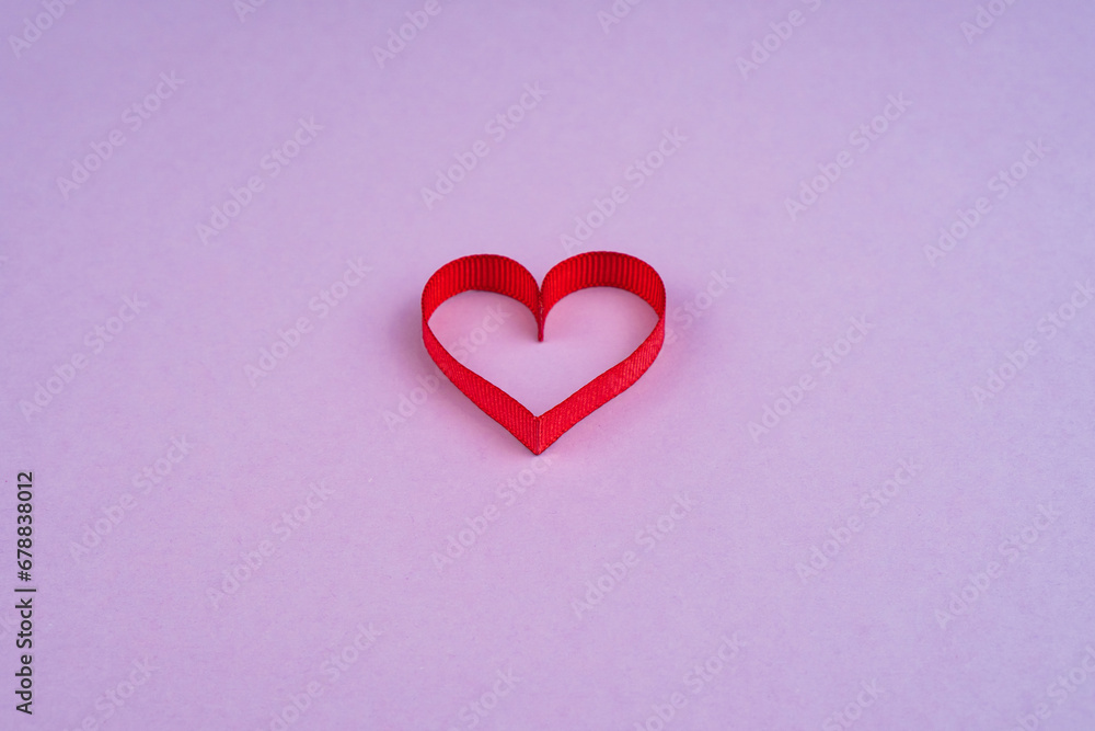 Top view Valentine's Day concept with copy space. Red ribbon heart on purple papper background Top view Valentine's Day concept with copy space. Red ribbon heart on purple papper background