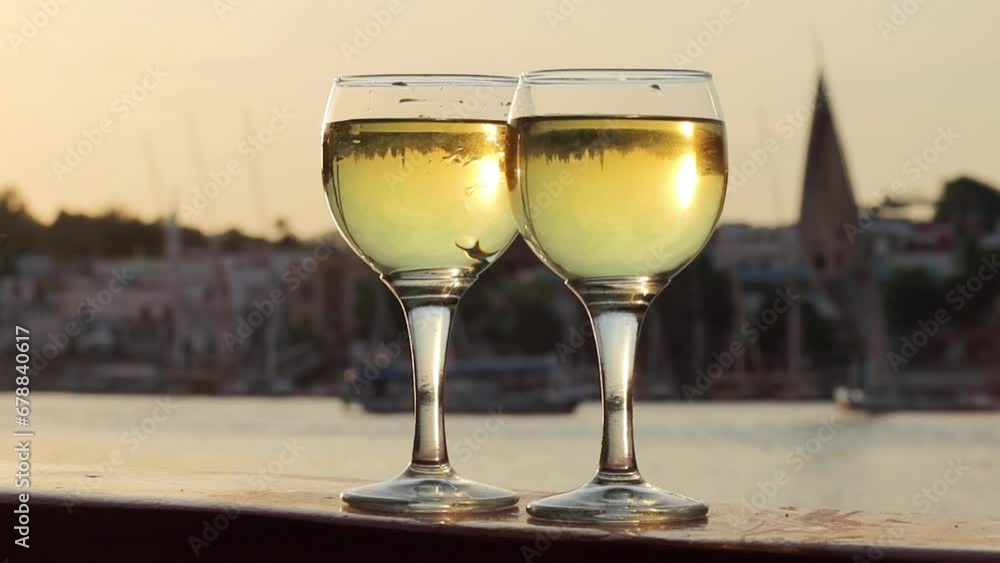 Two glasses of white wine with river view and boats on the background Two glasses of white wine with river view and boats on the background