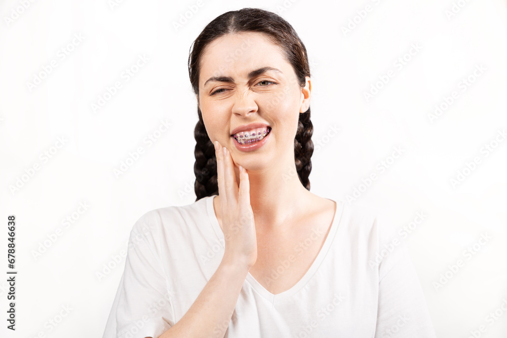 Portrait of Caucasian young woman with ligature braces on her teeth suffering of pain. White background. Concept of orthodontic treatment and malocclusion Portrait of Caucasian young woman with ligature braces on her teeth suffering of pain. White background. Concept of orthodontic treatment and malocclusion