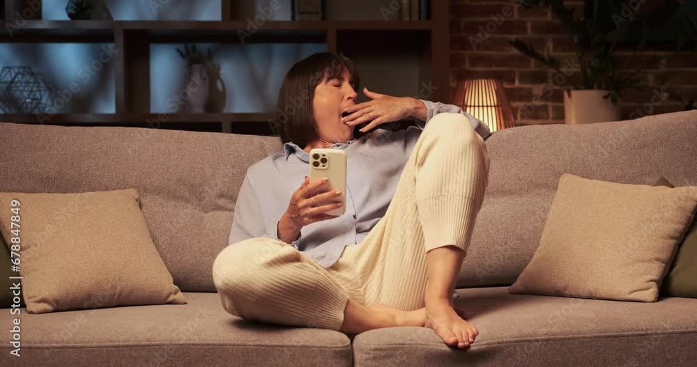 Woman lounges on the sofa, stifling a yawn born of sheer boredom. Phone lies in hands, its screen unable to capture interest. The room exudes an air of ennui as she searches for entertainment. Woman lounges on the sofa, stifling a yawn born of sheer boredom. Phone lies in hands, its screen unable to capture interest. The room exudes an air of ennui as she searches for entertainment.